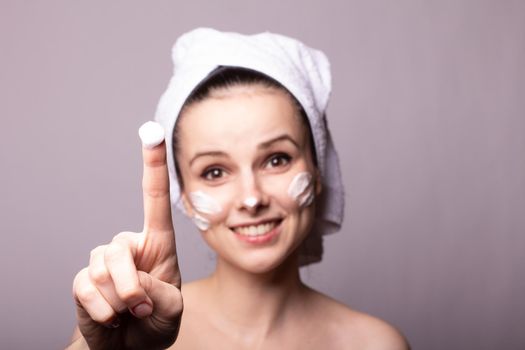woman in a white towel on her head with cream on her face, gray background. High quality photo