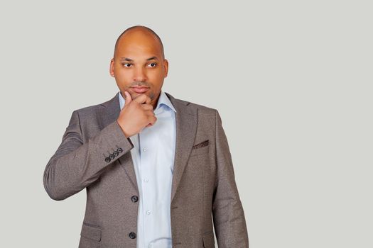 A smart, confident African American young man in a suit, holds his chin and looks thoughtfully to the side, thinking about his future.