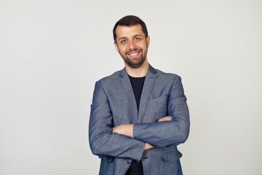 Young businessman with a smile man with a beard in a jacket, happy face, smiling with crossed arms, looking at the camera. A positive person. Portrait of a man on a gray background.