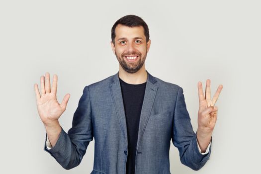 Young businessman man with beard smiling, showing number eight with fingers on hand, smiling confidently and happily, looking into the camera. The man shows eight fingers. Number 8.