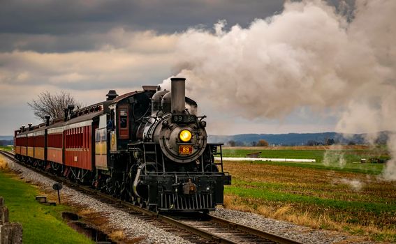Ronks, Pennsylvania, October 2020 - A Antique Restored Steam Engine and Coaches Approach Blowing Smoke and Steam Passing Thru Corn Fields on a Sunny Day