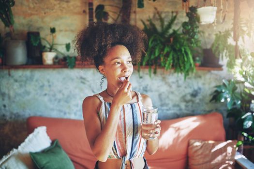 Shot of a beautiful African woman drinking medication in her living room - Stock Photo