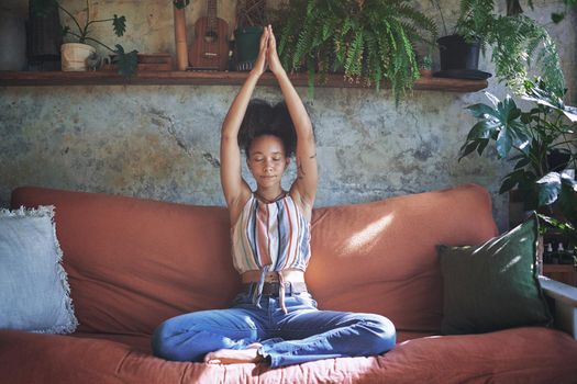 Shot of a beautiful African woman meditating on the sofa at home - Stock Photo