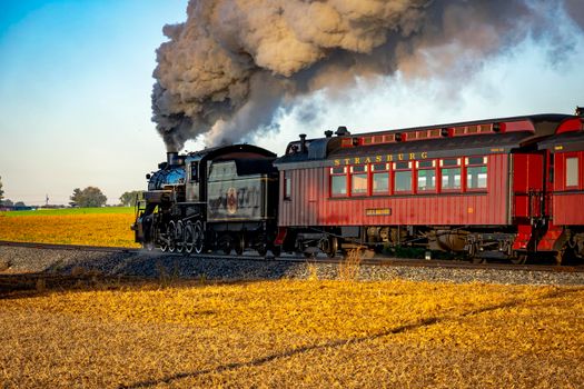 Ronks, Pennsylvania, October 2020 - A View of an Antique Passenger Steam Train Blowing Smoke Traveling Pass at Sunrise on a Beautiful Partly Cloudy Day