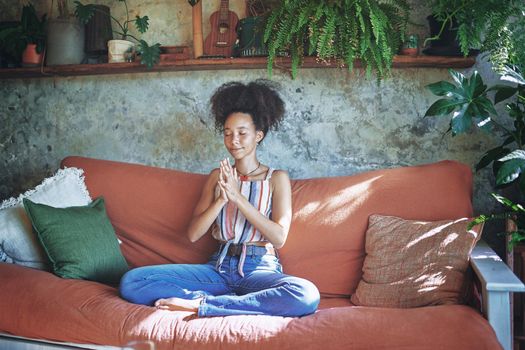 Shot of a beautiful African woman meditating on the sofa at home - Stock Photo