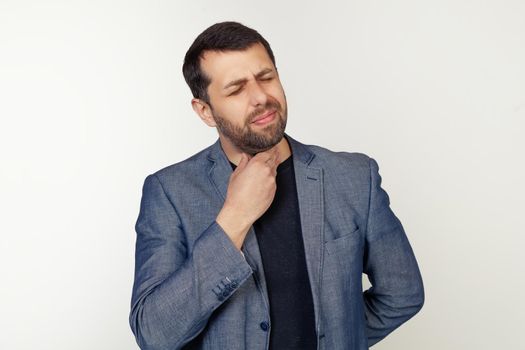 Young businessman man with beard touching painful neck, sore throat from flu, lump and infection. Portrait of a man on a gray background.