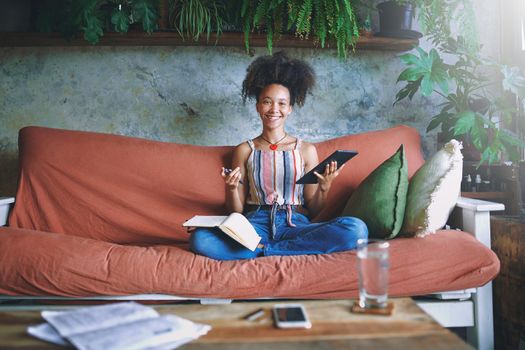 Beautiful African woman scrolling on her tablet and making notes in her living room