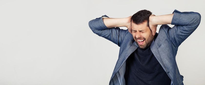 Young businessman man with a beard in a jacket. Hands on head, suffering from headache in despair and under stress due to pain and migraine. Portrait of a man on a gray background.