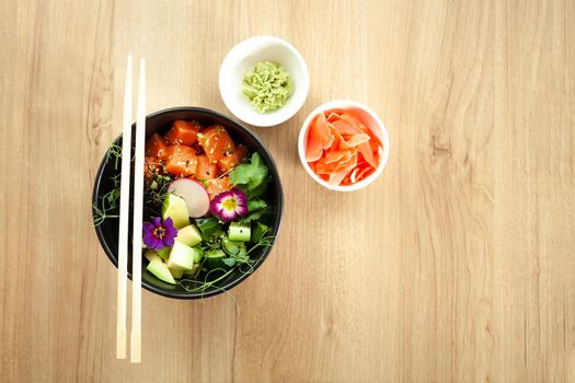 Poke salad with salmon in a bowl next to wasabi and ginger. Ingredients fresh salmon, avocado, cucumber, rice, Tamarind sauce mango sauce nori lime, sesame seeds, cilantro. Asian seafood salad concept