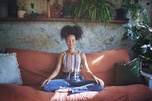 Shot of a beautiful African woman meditating on the sofa at home - Stock Photo