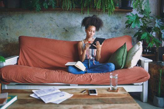 Beautiful African woman scrolling on her tablet and making notes in her living room