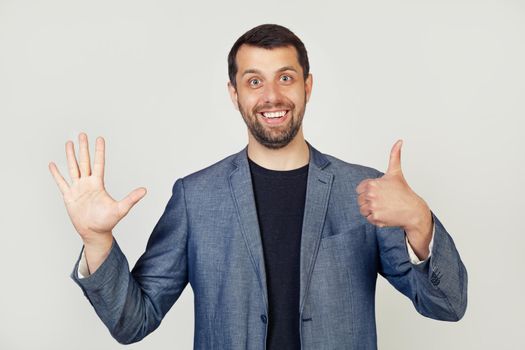Young businessman man with beard smiling, showing number six with fingers on hand, smiling confidently and happily, looking into the camera. The man shows six fingers. Number 6.