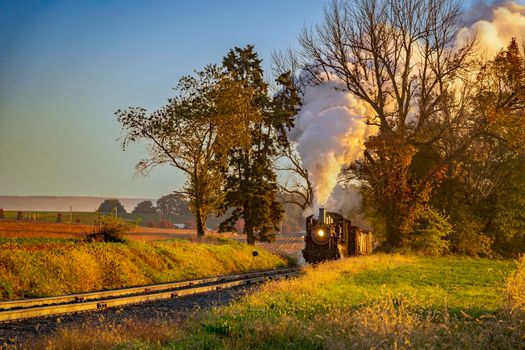 A View of an Antique Freight Steam Train Blowing Smoke Approaching Thru Trees in Late Afternoon