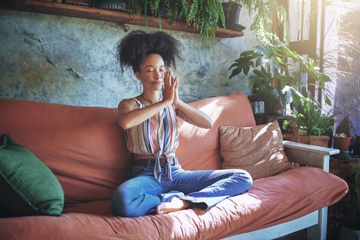 Shot of a beautiful African woman meditating on the sofa at home - Stock Photo