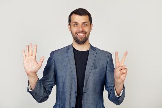Young businessman man with beard smiling, showing number seven with fingers on hand, smiling confidently and happily, looking into the camera. The man shows seven fingers. Number 7.