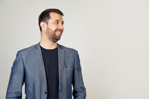 Closeup of a handsome bearded guy in a jacket standing in profile, looking to the side, posing for a photo. A man looking away to the side with a smile on the face, natural expression.
