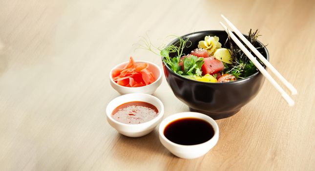 Poke salad with tuna in a bowl. Ingredients fresh tuna, cherry tomatoes, marinated seaweed, rice, takuan, Ponzu sauce, Teriyaki sauce, nori, sesame seeds, lime, cilantro. Asian seafood salad concept