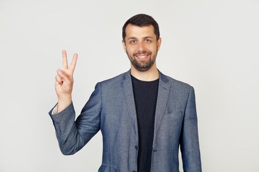 Young businessman man with beard smiling, showing number two with fingers on hand, smiling confidently and happily, looking into the camera. The man shows two fingers. Number 2.