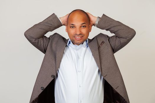 Portrait of an upset young African American guy businessman looking at the camera holding hands in his head. Standing on a gray background