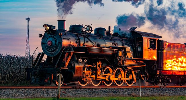 Ronks, Pennsylvania, October 2020 - A View of an Antique Steam Passenger Train Approaching at Sunrise With a Full Head of Steam and Smoke Traveling Thru Farmlands