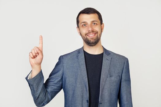 Young businessman man with beard smiling, showing number one with fingers on hand, smiling confidently and happily, looking into the camera. The man shows one finger. Number 1.