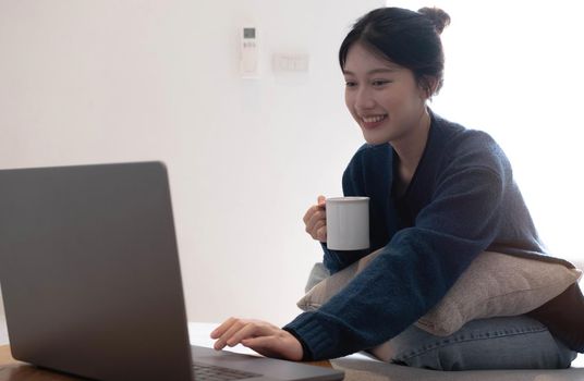 Portrait of smiling happy cheerful beautiful pretty asian woman relaxing drinkand use laptop. Girl felling enjoy having breakfast in holiday morning vacation on sofa at home.