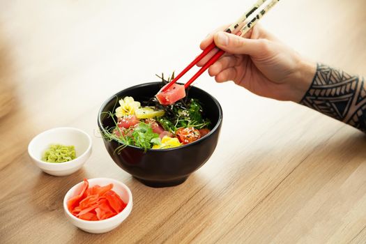 A man eats a Poke salad with tuna in a bowl with chopsticks. Place the tuna salad in a bowl. Young man guy in a restaurant eating poke salad. Asian seafood salad concept