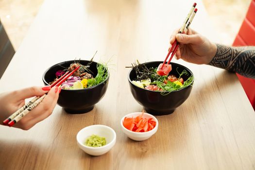 Loving couple man and woman eating salad poke chopsticks. Place the tuna salad in a bowl. People in the restaurant eat salad with chopsticks. Asian seafood salad concept
