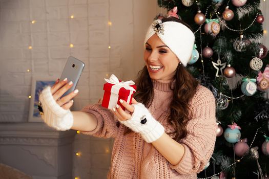 Woman with gift box communicating by mobile phone smartphone online call. Remote celebration of Merry Christmas and New Year in quarantine coronavirus covid 19. Social distance, remote communication.