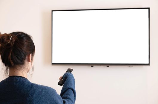 behind of asian young woman watching white screen TV on the sofa and using the remote at home