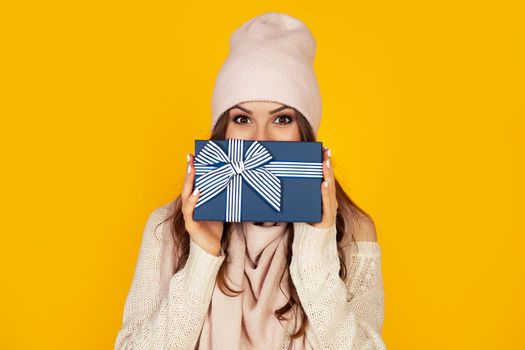 Happy young woman with a gift box in her hands, covers half of her face with a New Year's gift. The girl shows a gift to the camera. The concept of gifts and surprises for the new year and christmas.