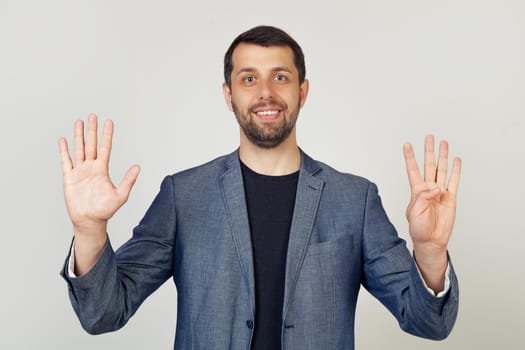 Young businessman man with beard smiling, showing number nine with fingers on hand, smiling confidently and happily, looking into the camera. The man shows nine fingers. Number 9.