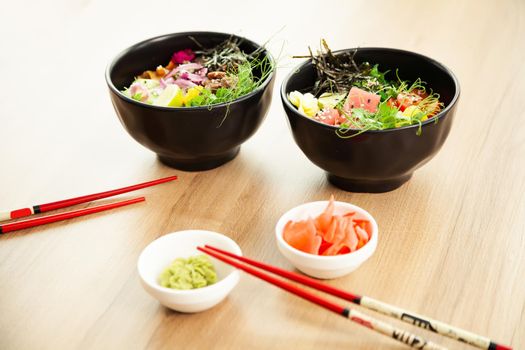 Two poke salads with beef and tuna in a bowl on a restaurant table. Poke salads in a bowl next to chopsticks and ginger with wasabi. Asian salad concept.