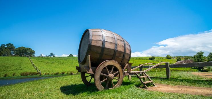 Wine barrel on cart against green grass field in countryside agriculture landscape background. Organic food, winery and alcohol drinks product industry.