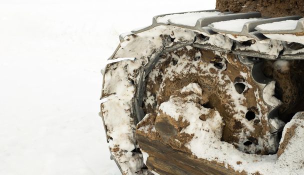 The metal tracks of a bulldozer tractor in winter clears the road from snow. On a frosty day, a yellow bulldozer in winter