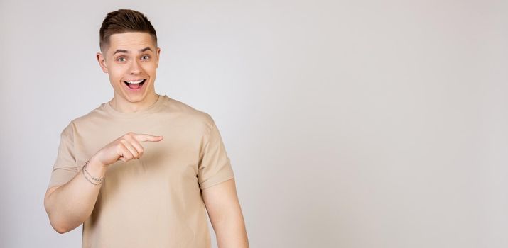 The man points to the side and smiles. Photo of young attractive excited handsome modern freelancer, entrepreneur, employer student looking at camera, pointing with index finger to copy space.