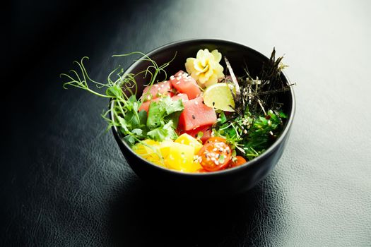 Poke salad with tuna in a bowl. Ingredients fresh tuna, cherry tomatoes, marinated seaweed, rice, takuan, Ponzu sauce, Teriyaki sauce, nori, sesame seeds, lime, cilantro. Asian seafood salad concept
