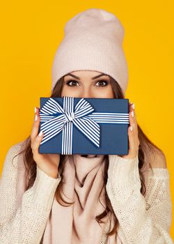 Happy young woman with a gift box in her hands, covers half of her face with a New Year's gift. The girl shows a gift to the camera. The concept of gifts and surprises for the new year and christmas.