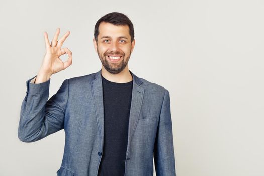 Handsome, confident young man guaranteeing impeccable quality, shows a well-confirming gesture, smiles, satisfied, approves a good idea, recommends a promo agrees with you stands on a white background