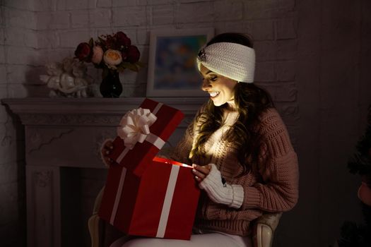 Happy young woman with a present, opening a Christmas present box. Portrait of happy smiling girl opening gift box isolated on red background