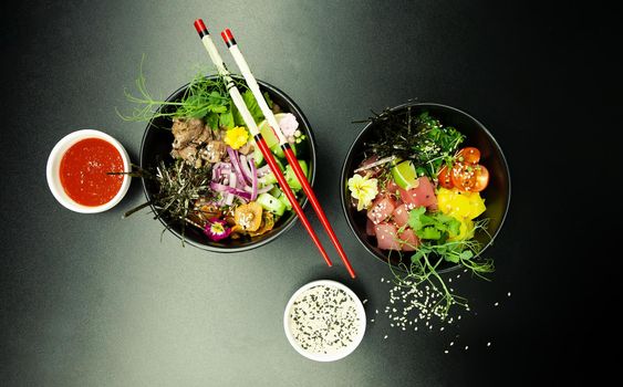 Poke salads with tuna and beef in bowls on the table. Two bowls of poke salad with chopsticks on a gray background. Asian seafood salad concept.