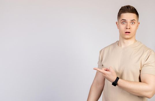 The man the guy points to the side with a displeased face. Young doubter man, holds his hand and points to the side with forefingers at blank space