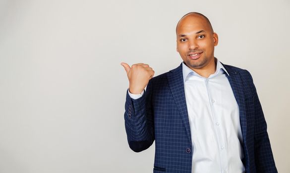 Young African American man smiling positively, smiling with happy face, looking and pointing to the side with thumb up. Black man.