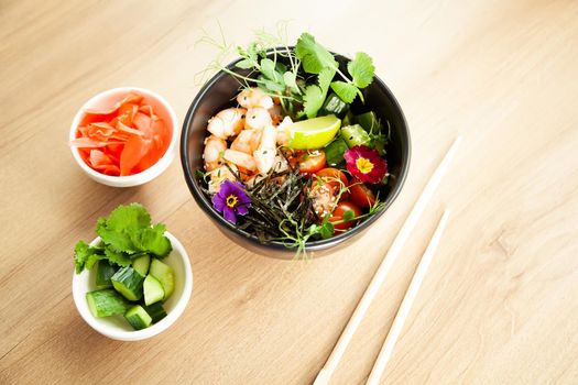 Poke salad with shrimp in a bowl. Ingredients Shrimp, blanched spinach, cherry tomatoes, rice, cucumber, soy-ginger sauce, Spicy sauce, nori, sesame, lime, cilantro. Asian seafood salad concept