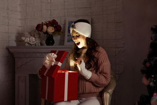 Happy young woman with a present, opening a Christmas present box. Portrait of happy smiling girl opening gift box isolated on red background