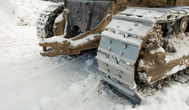 The metal tracks of a bulldozer tractor in winter clears the road from snow. On a frosty day, a yellow bulldozer in winter