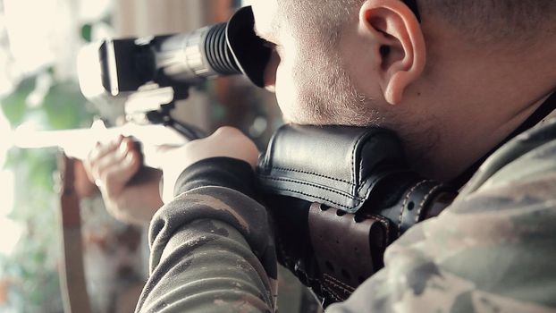 A man with a gun is aiming and looking at the sight. The carbine is aimed to prepare for a firearm shot. Man in camouflage clothing.
