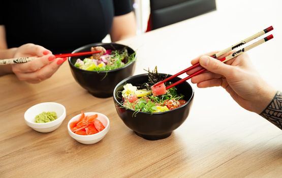 A man adds soy sauce to Poke salad. Guy young man dressing salad with sauce in a restaurant or cafe