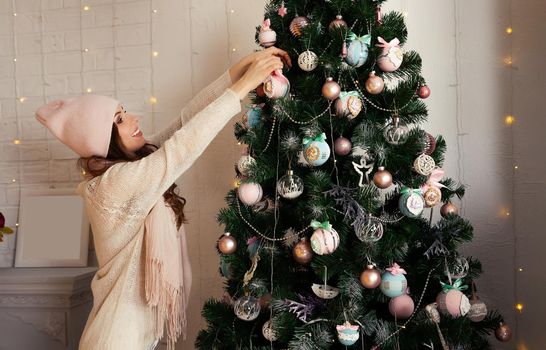 Happy young woman decorates the Christmas tree hang the ball on the tree. Christmas decoration, toys hanging on the tree, Christmas tree ball. New year and christmas holiday concept