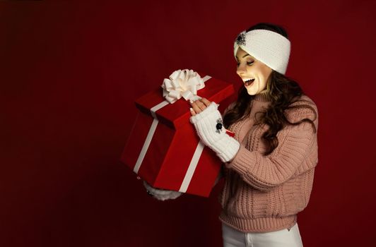 Happy young woman with a present, opening a Christmas present box. Portrait of happy smiling girl opening gift box isolated on red background